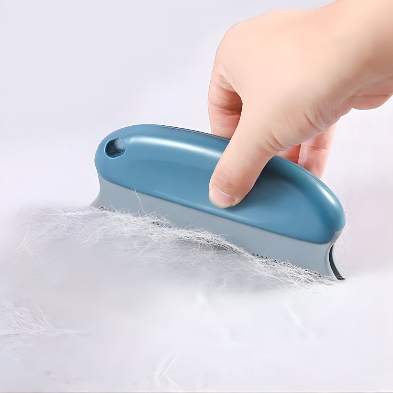 Blue grooming brush being used on a white surface with visible hair.